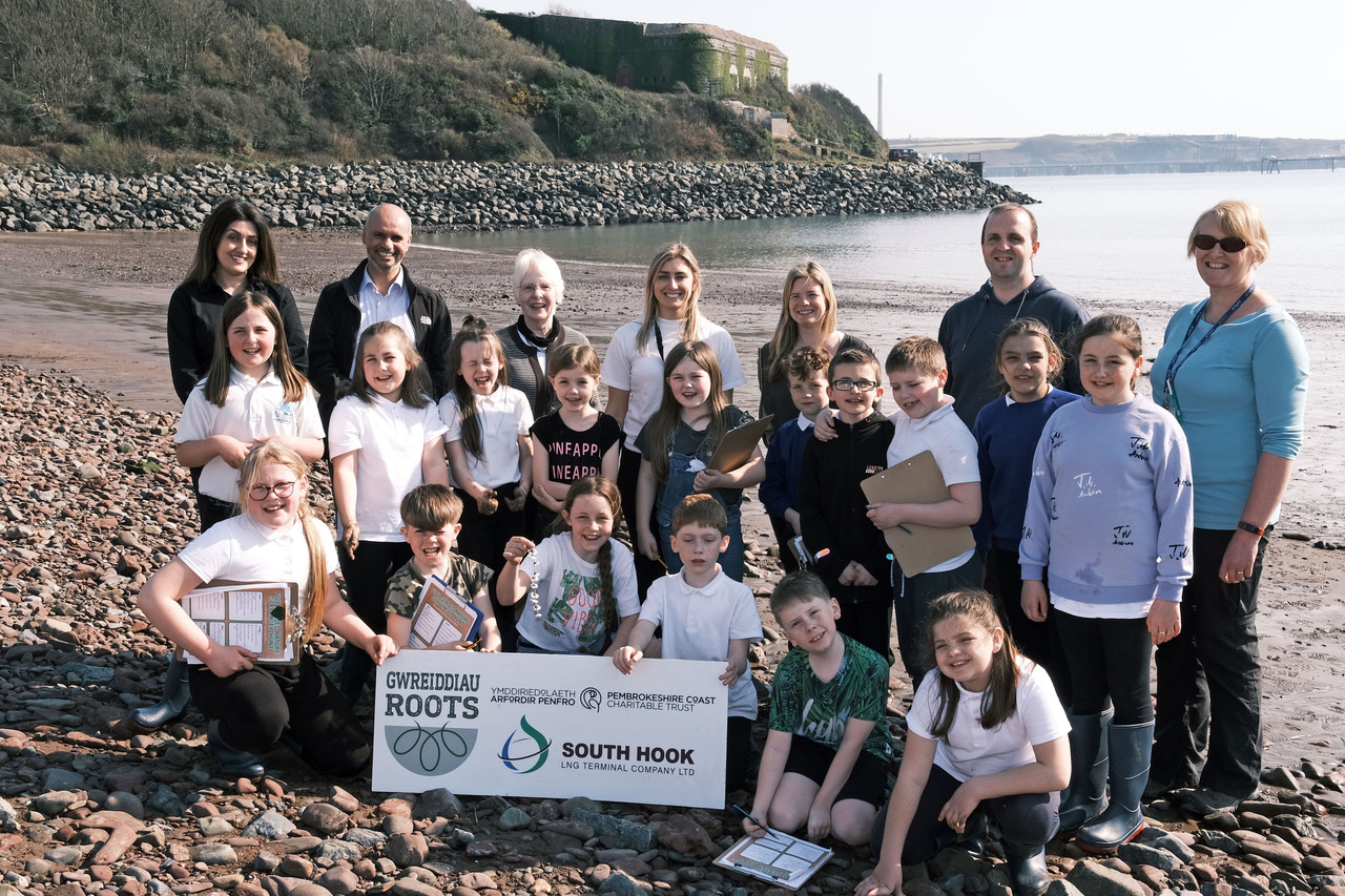 A group photo including school children involved in the project and representatives from both South Hook LNG and Pembrokeshire Coast National Park Trust. They are stood on the beach in Gelliswick Bay with the sea in the background.