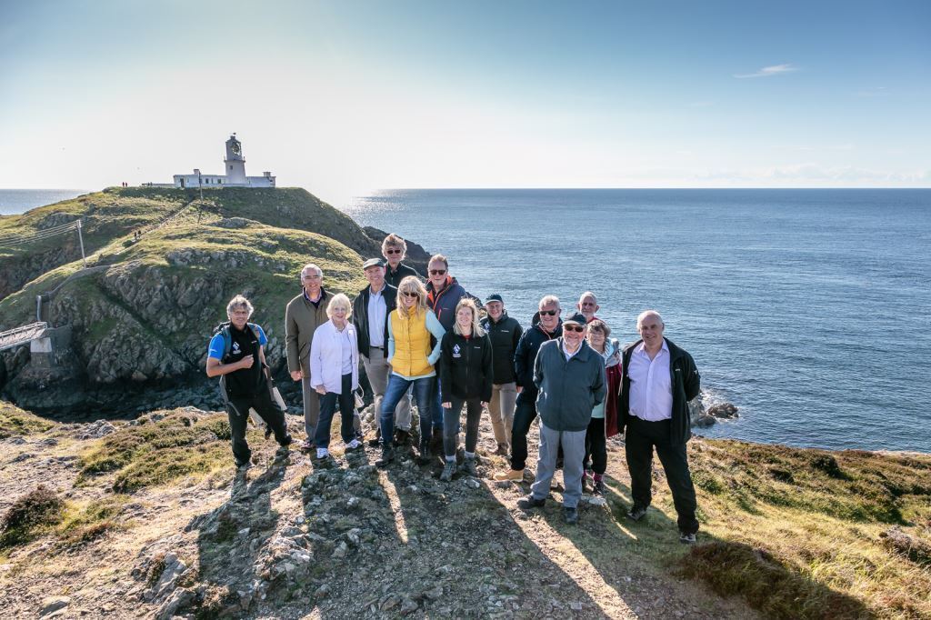 A group of people pictured with the sea and a lighthouse in the background 