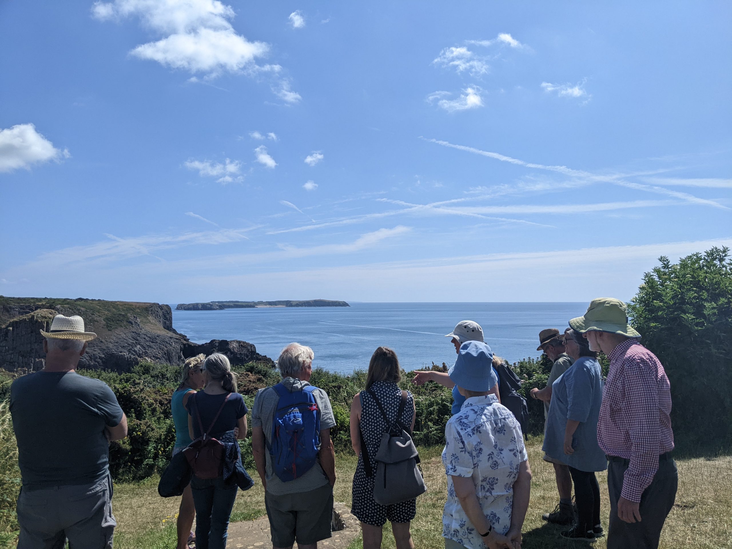 A group of individuals overlooking a beautiful view of the sea, cliffs and caldey island in the distance.